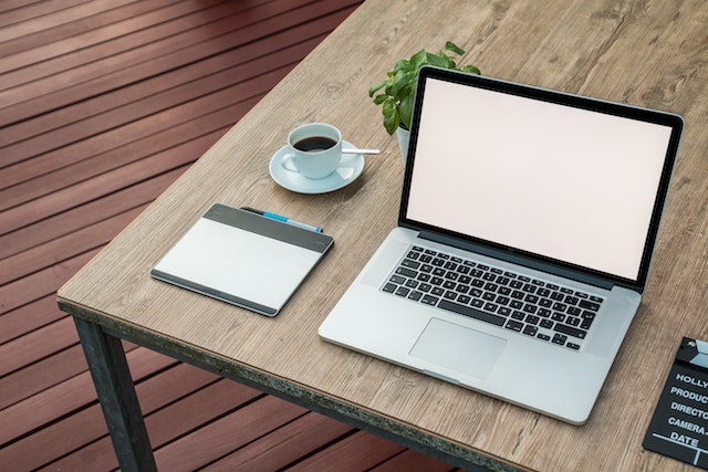 computer-on-a-wood-desk-next-to-a-notepad-and-a-cup-of-coffee